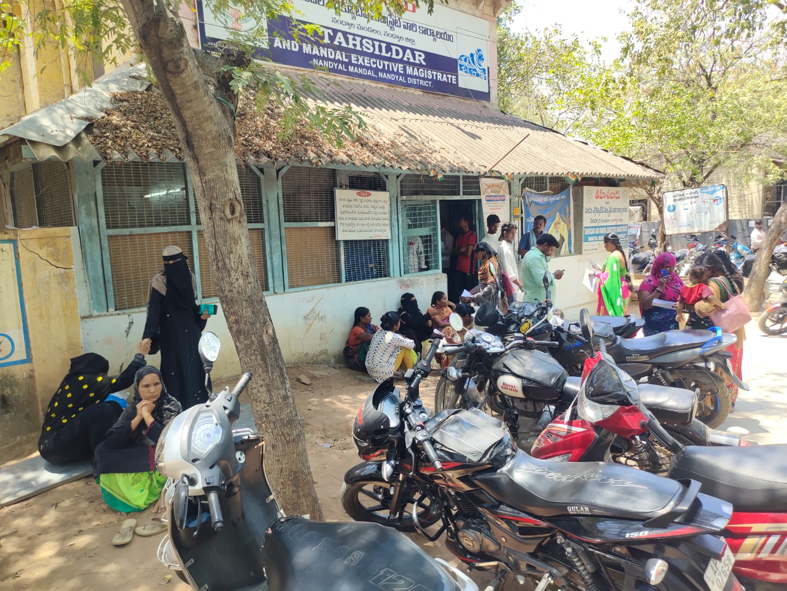 తాహసీల్దార్ కార్యాలయం ముందు అలసిపోయి క్రింద కూర్చున్న మహిళలు.